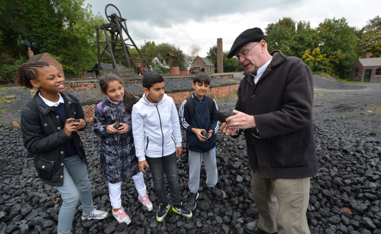 Four school children hold pieces of coal at the reconstructed colliery at the Black Country Museum. Next to them, a member of staff shows them a piece of coal