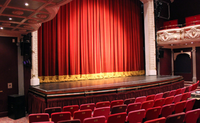 A view of the auditorium of the Theatre Royal Winchester. Rows of red fold up seats facing a stage with a red curtain