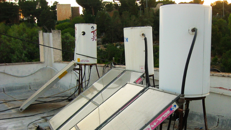 Three solar boilers on a rooftop - white cylinders on a tripod, connected to a panel