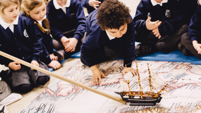 A group of primary school children crouch down to look at a map and a model of a ship