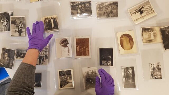 A pair of hands wearing purple gloves arranges black and white photos from the Holocaust Survivors' Friendship Association