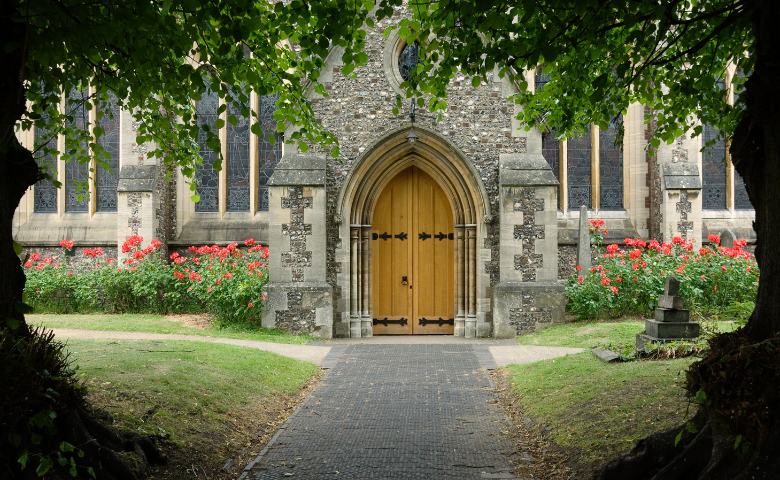 Funding for places of worship - JayKay57 via Getty Images The wooden front door of a stone church, framed by trees