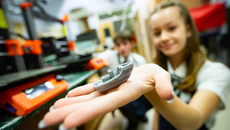 A student at Ysgol Maes Garmon holds out her hand to show a small grey plastic boat that she has 3D printed