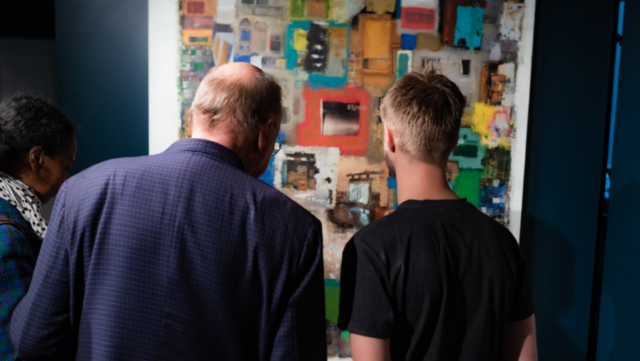 A group of people look at a colourful artwork displayed on the wall.
