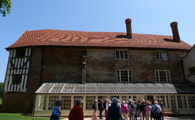 The image shows a restored historic building with a glass conservatory. A group of people stand outside preparing to enter the building.
