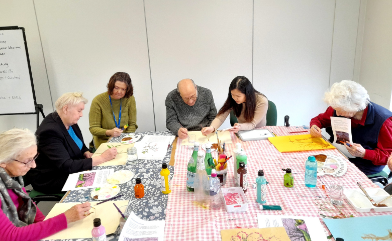 A group of older people are sat around a table taking part in craft activities.