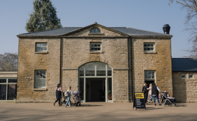 The image shows a stone building with a large front door that stands open. Families are walking into the open door.