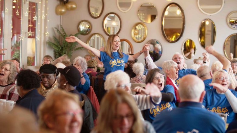 Golden Oldies singing session A group of older people in blue T-shirts at a Golden Oldies singing session. The leader is waving their arms in the air