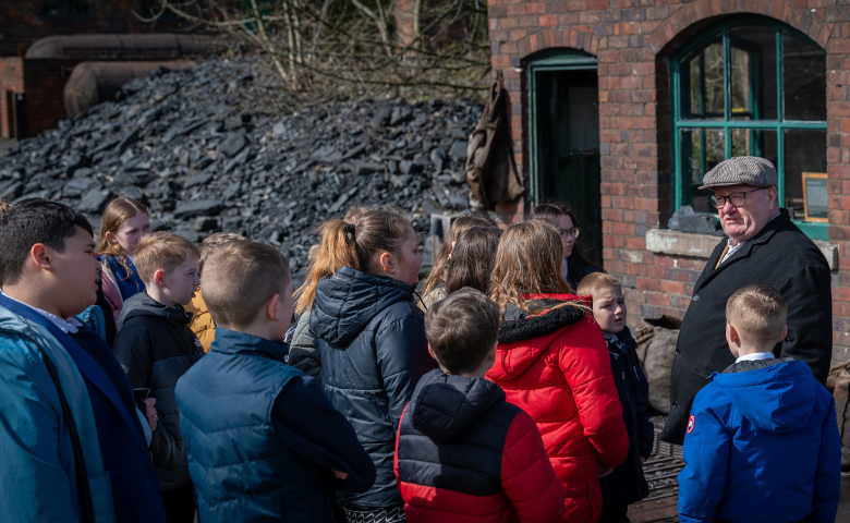 A group of schoolchildren listening to a man talking about the museum behind him. 