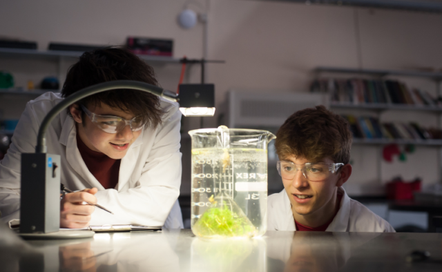 Two students wearing goggles watch a science experiment in a laboratory.