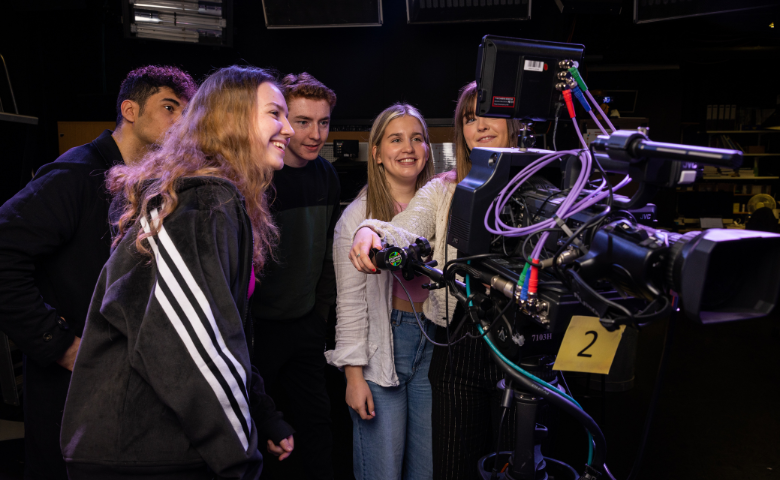 Five students look at a screen on the back of a large camera.