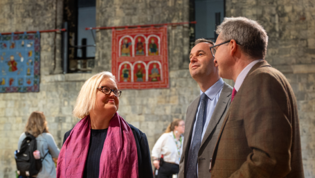Baroness Twycross, Paul Ramsbottom and Dr Tim Pestell in Norwich Castle. Behind them are wall hangings on the inside castle wall.
