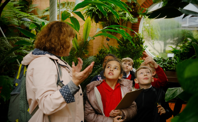 Photo credit Irina Mackie, image owned by Birmingham Botanical Gardens A school teacher gestures to a group of children, surrounded by plants in Birmingham Botanical Gardens.